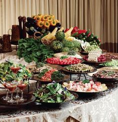 a table full of different types of food on plates and serving trays with wine glasses