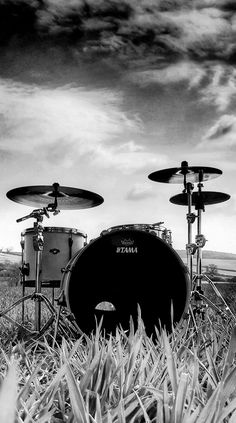 black and white photograph of drums in front of a drum set on the grass with cloudy sky