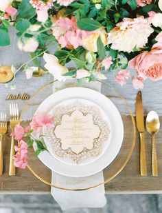 a place setting with gold and white plates, silverware and pink flowers on the table