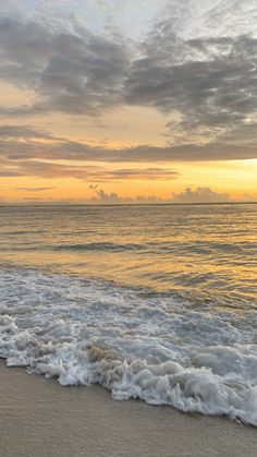 an ocean beach with waves coming in to shore and the sun setting on the horizon