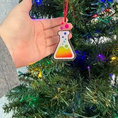 a hand holding a colorful ornament in front of a christmas tree