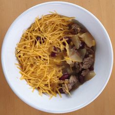 a white bowl filled with meat and cheese on top of a wooden table next to a fork