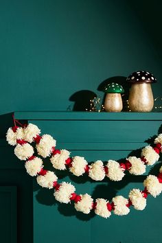 white and red pom - poms are hanging from the mantle in front of green walls