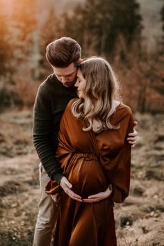 a pregnant couple cuddling in the woods at sunset