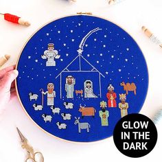 a cross stitch christmas scene with the birth of jesus and baby jesus on it, surrounded by crochet needles