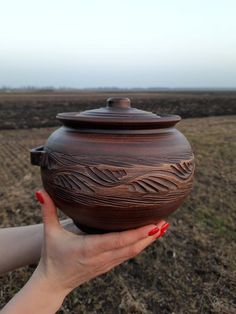 a woman's hand holding a brown pot in front of a field