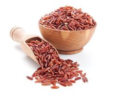 a wooden bowl filled with red rice next to a wooden scoop full of brown rice