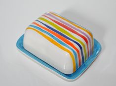 a multicolored striped cake sitting on top of a blue plate next to a white wall