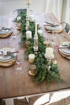 the table is set with candles, plates and greenery on it for christmas dinner