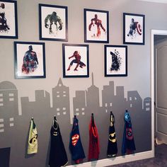 the wall is decorated with superheros and batman capes hanging on it's hooks