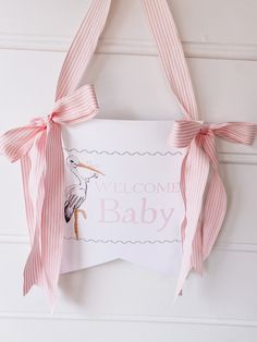 a welcome baby sign hanging on the wall with pink ribbon around it and a stork