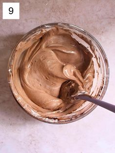 a glass bowl filled with chocolate frosting on top of a white counter next to a spoon