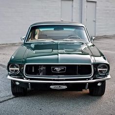 an old green mustang sitting in front of a garage door on the side of a road