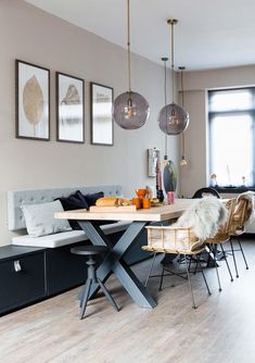 a dining room table and chairs in front of a window with hanging lights above it