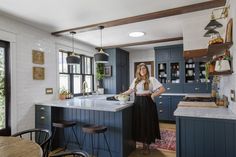 a woman standing in the middle of a kitchen with blue cabinets and an island counter