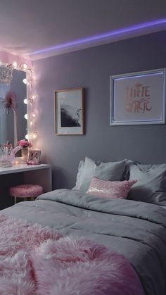 a bedroom decorated in pink and grey with lights on the wall, vanity table and bed