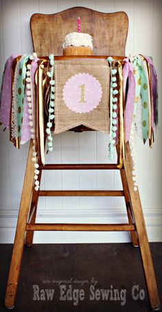 a wooden high chair with a cupcake on it's back and some ribbons around the seat