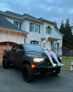 a man sitting on the hood of a black truck in front of a large house