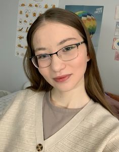 a woman wearing glasses and a sweater in a room with pictures on the wall behind her