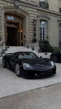 a black sports car is parked in front of a large building with steps leading up to it