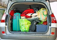 the back end of a silver van filled with luggage and other items, including bags