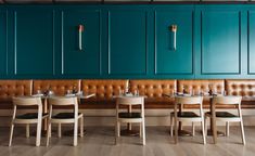 a restaurant with teal green walls and leather booths, wooden tables set up in front of them