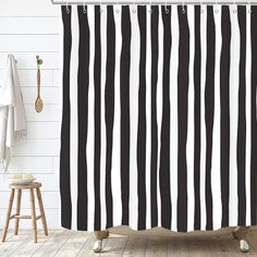 a black and white shower curtain hanging on a wall next to a wooden stool in a bathroom