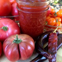 tomatoes, peppers and other vegetables sit on a table next to a jar of ketchup