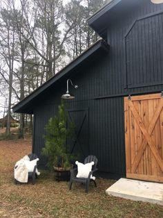 two chairs sitting in front of a barn with a tree and lamp on the side