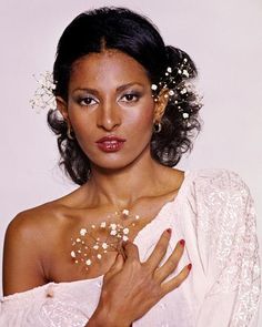 a woman with flowers in her hair wearing a white dress and posing for the camera