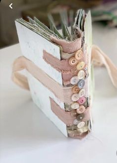 an open book with buttons on it sitting on top of a white table next to other books