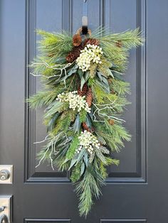 a wreath with pine cones and white flowers hangs on the front door