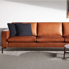 a brown leather couch with three pillows on it's back and two side tables