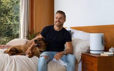 a man sitting on top of a bed next to a brown dog laying on it's side