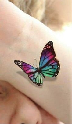 a woman's arm with a colorful butterfly tattoo on it, while she is covering her face