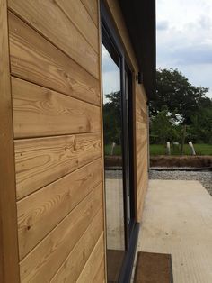 the side of a building with wooden siding and windows on it's sides, looking out onto an open field