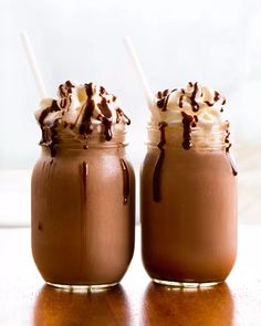 two chocolate milkshakes with whipped cream and chocolate drizzles on top