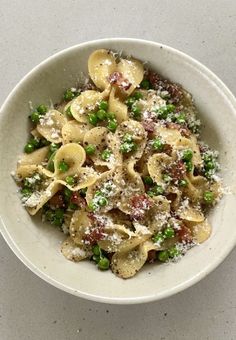 pasta with peas and parmesan cheese in a white bowl on a gray surface