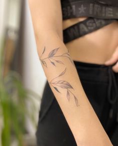 a close up of a person with a tattoo on their arm and behind her is a plant