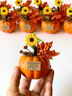 a hand holding a small pumpkin decorated with flowers and leaves in front of rows of fake sunflowers