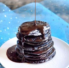 a stack of chocolate pancakes on a white plate with syrup drizzled over the top