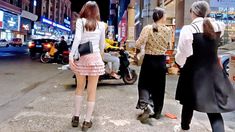 three people are walking down the street with scooters and motorcycles in the background