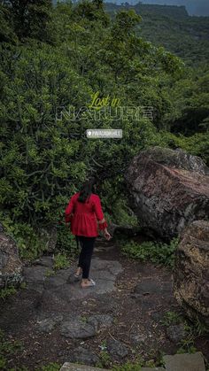 a woman in red jacket walking up a hill with trees and rocks behind her on a cloudy day