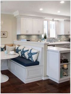 a kitchen with white cabinets and blue pillows on the bench in front of the table