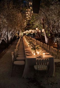 a long table is set up with candles and chairs for an outdoor dinner in the evening