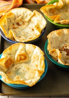 four bowls filled with food sitting on top of a metal pan covered in tortilla shells