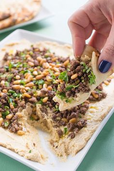 a person dipping some kind of food on top of hummus