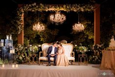 a bride and groom sitting on a couch under a chandelier at their wedding