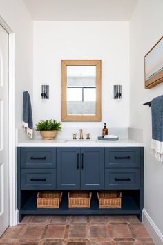 a bathroom with blue cabinets and white walls, brown tile flooring and a large mirror above the sink