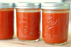 three jars filled with red sauce sitting on top of a wooden table